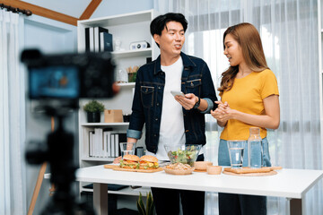 Chef influencers reading comment on phone for answer time on social media cooking show channel live streaming menu dish mix salad, bun bread wholegrain and hamburger record by video camera. Infobahn.