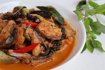 Sliced ​​giant catfish meat Stir-fried spicy red curry, brinjal eggplant, basil leaves, fresh pepper in a plate on a white background

