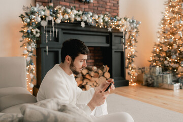 Happy man using smart phone home alone celebrating virtual Christmas video calling family and...