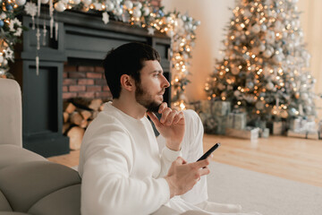 Happy man using smart phone home alone celebrating virtual Christmas video calling family and friend. Virtual holiday gathering online, normal and social distancing. Part of a series