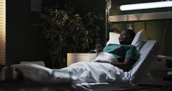 Cheerful but powerless African girl lies in the hospital in an oxygen tube looking at photos on the phone while being treated.