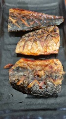 Grilled saba fish on a black plate in a Japanese restaurant