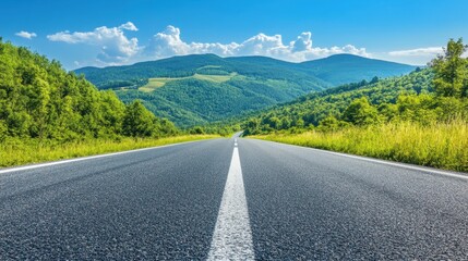 Naklejka premium Empty asphalt road stretching towards a range of green mountains under a clear blue sky, perfect for nature and travel concepts.