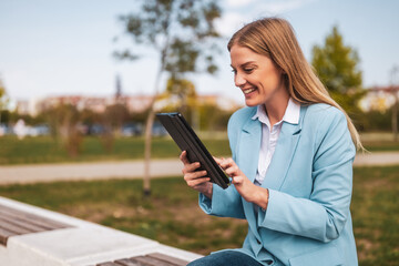 Fototapeta premium Beautiful businesswoman using digital tablet while sitting on the bench outdoor. 