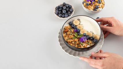 Women's hands hold a bowl of Greek yogurt, granola and berries. Breakfast. Copy space