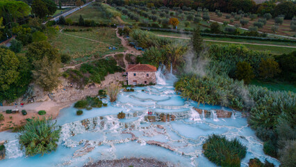 Relax in the soothing waters of Saturnia thermal baths, surrounded by the lush greenery of Tuscany Italy where steam gently rises from the warm springs creating a serene atmosphere.