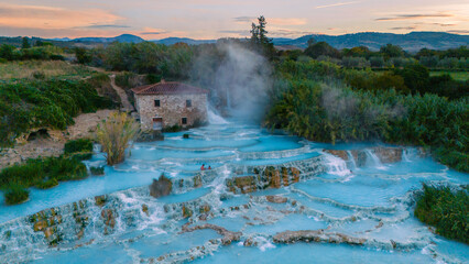 Visitors relax in Saturnia's soothing thermal waters, surrounded by lush landscapes and gentle waterfalls, creating a magical atmosphere of tranquility on a serene Tuscany Italy evening