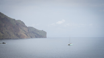 Fototapeta premium Small sailboat with its sails down near the coastal cliffs, Madeira, Portugal