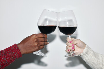 Close-up of two individuals raising wine glasses in cheerful toast, highlighting ethnic diversity and festive spirit, captured against minimalist background