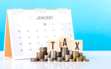 A wooden block labeled 'TAX' sits beside a stack of coins and a calendar. Represents concept of...