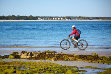 active senior woman cycling with her electric mountain bike along the beach of Loctudy, Brittany,...