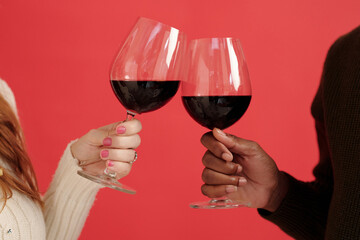 Close-up of two people holding glasses of red wine, creating a toast gesture against a red background under warm lighting
