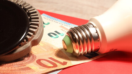Primo piano del costo del gas e dell'elettricità della lampadina e del gas con banconote in euro e sfondo rosso.