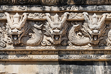Ornate carvings of dragon faces on an ancient stone wall display detailed craftsmanship and cultural significance

