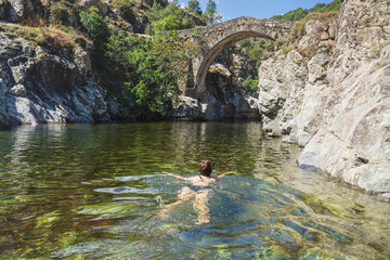 Young woman is bathing in a river at the historic Genoese bridge in Asco, Corsica