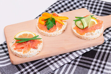 Rice Cake Sandwiches with Fresh Salmon, Cucumber, Yellow Paprika and Greens on Wooden Cutting Board. Diet Food. Quick and Healthy Sandwiches. Crispbread with Fresh Fillings. Healthy Dietary Snacks