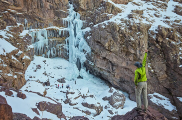 hiker near a frozen Waterfall near Jebel Toubkal peak, Atlas mountains, Morocco