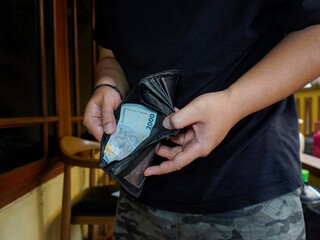 A close-up of a man's hand realizing that his wallet is empty only contains one 2.000 Indonesian...