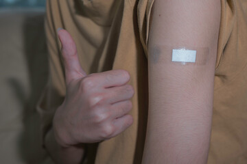 Asian man showing his shoulder with bandage after getting a vaccination during covid-19 immunization program. concept of recommended inoculation, vaccination, vaccinated patient, vaccine roll-out 