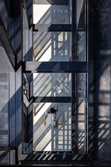 Architecture details of view from top through the steel columns and beams structure with a woman walking across in the strong light and shadow.