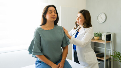 Female Hispanic patient inhaling while her doctor is listening to her breathing during a medical...