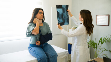 Doctor showing and explaining x-ray scan results to young injured patient wearing neck brace and...