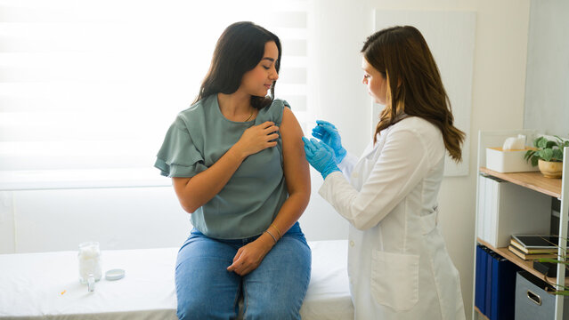 Latin female patient is getting vaccinated by a doctor wearing gloves in a medical office