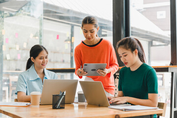 Collaborative women working together in modern office space, using laptops and tablet. They are engaged in productive discussion, showcasing teamwork and creativity