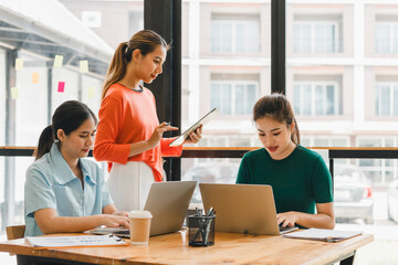 Collaborative workspace with three women engaged in productive meeting, using laptops and tablet. bright environment enhances focus and teamwork