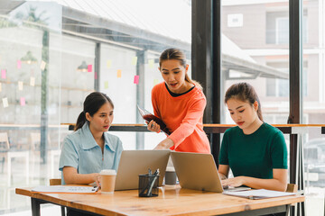 Collaborative meeting among three women in modern workspace, discussing ideas while using laptops....