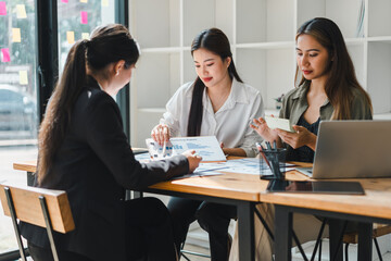 Collaborative business meeting with three women discussing financial reports and strategies. They are engaged in productive conversation, analyzing data on documents and digital devices