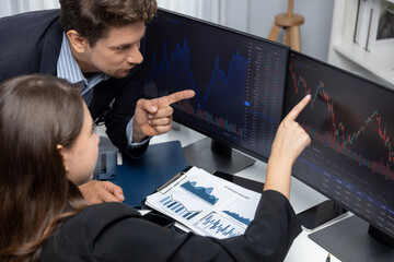 Two business traders discussing value business statistic graph company on paper report analyzing with dynamic stock exchange market currency real time website surround pc screens at office. Postulate.