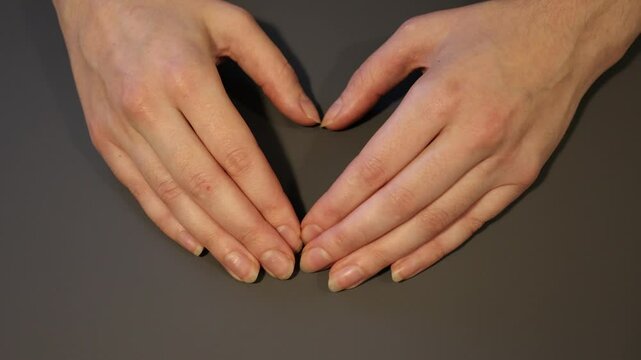 Female hands with natural nails shaped as a heart. Gray background. 