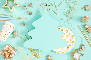 Christmas background. Festive scene with golden ornaments, cut-out silhouette of Christmas tree, plates, cutlery, candles and confetti creating festive atmosphere on pastel green background