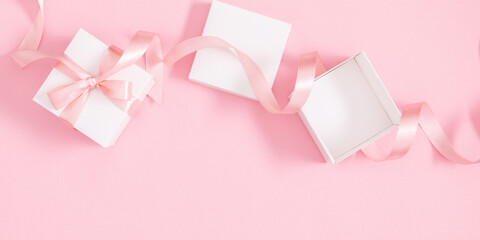 Pink festive setting. Open gift box and satin ribbon on soft pink background. Flat lay, top view,...