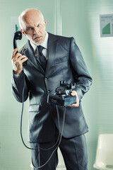 Confused senior businessman holding landline phone in office
