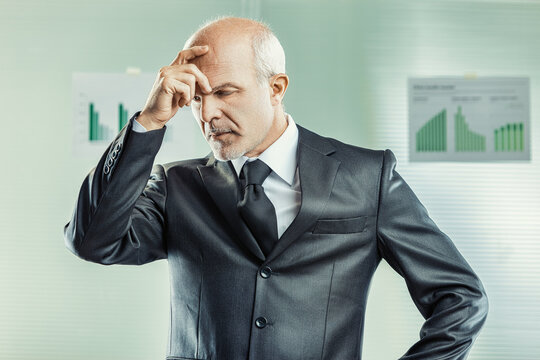 Businessman touching forehead in thought looking at charts