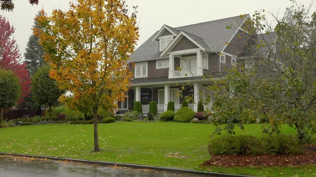 Establishing shot. Two story stucco luxury house with big tree and nice landscape at fall rainfall in Vancouver, Canada, North America. Day time on October 2024. ProRes 422 HQ.