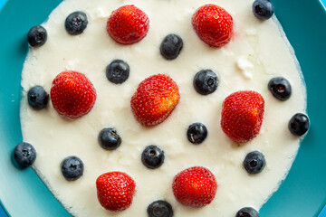 Berries strawberries and blueberries in a blue plate with thick whipped cream top view