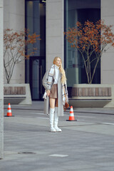 A stylish woman stands confidently in an urban landscape during a cool autumn afternoon waiting for...
