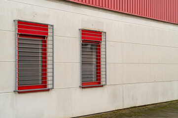 Fototapeta premium Two windows are protected by red and gray security bars on white wall