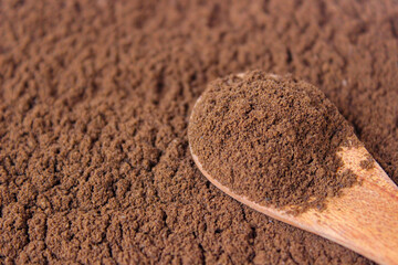 Roasted coffee powder on wooden spoon with coffee powder background, food background. closeup.