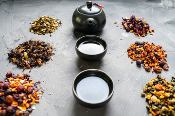Dry tea of different varieties and a teapot with cups on a gray background. Tea ceremony, Tea with...
