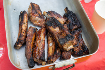 A metal tray full of quite burnt meat: a bunch of pork ribs are waiting to be eaten by a hungry group of friends.
