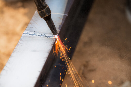Skilled welder cuts metal with a gas torch in industrial workshop. Sparks fly during precision fabrication process. Craftsman control and expertise in metalworking. Gas torch cuts through steel.