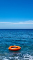 Obraz premium Orange Lifebuoy Floating in the Calm Blue Ocean