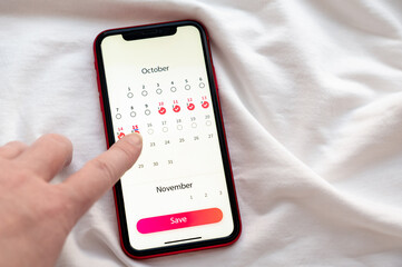 The phone display is a close-up where a woman marks the days of her menstrual cycle on a calendar
