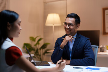 Two coworkers smiling and discussing a project, working together in the office at night