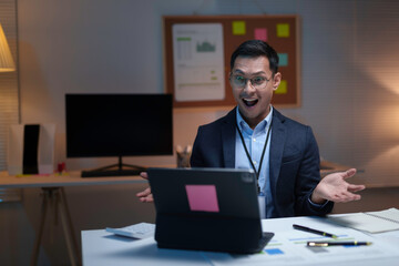Asian businessman is looking surprised at his laptop while working late in his office