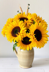 Fototapeta premium Bright yellow sunflowers arranged in a ceramic vase, creating a cheerful and vibrant display. Perfect for adding a touch of nature and warmth to any space.